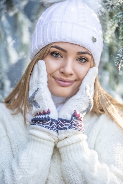 Une jolie fille touche la peau douce de son visage avec des gants d'hiver, vêtue d'un pull et d'un bonnet.
