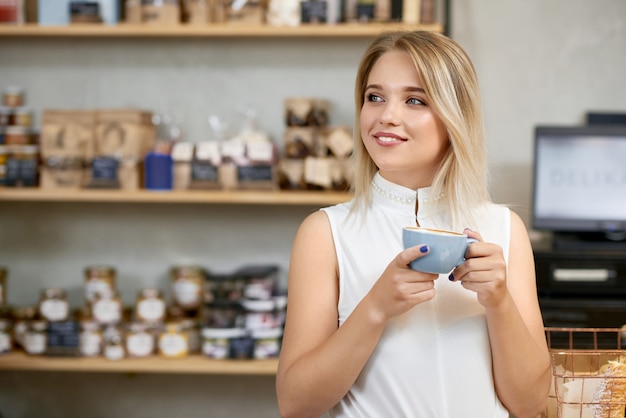 Jolie fille en train de boire du café en magasin, regardant de côté.