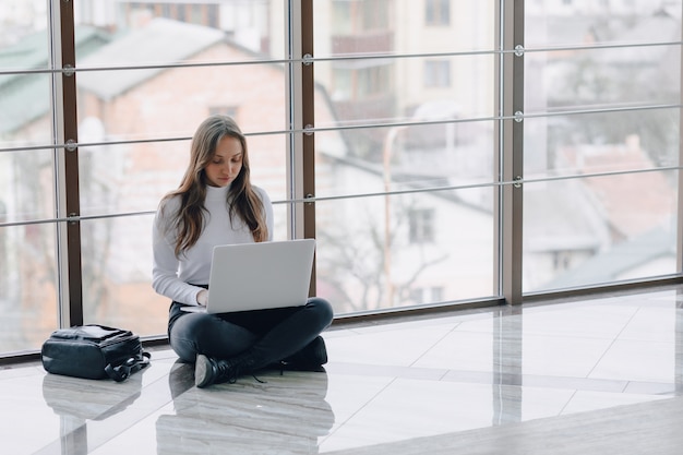 Jolie fille travaillant avec un ordinateur portable et des choses dans le terminal de l'aéroport ou un bureau au sol. atmosphère de voyage ou atmosphère de travail alternative.