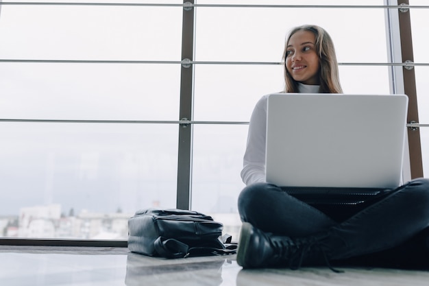 Jolie fille travaillant avec un ordinateur portable et des choses dans le terminal de l'aéroport ou un bureau au sol. atmosphère de voyage ou atmosphère de travail alternative.