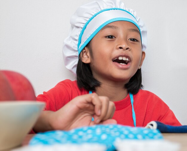 Jolie fille en uniforme de chef et jouets de cuisine simulés dans le comptoir de la cuisine