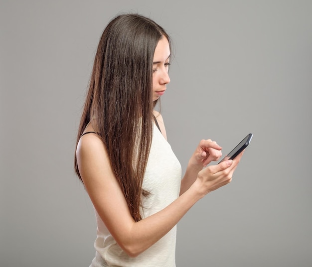 Jolie fille utilisant son smartphone pour envoyer des SMS isolé sur fond gris