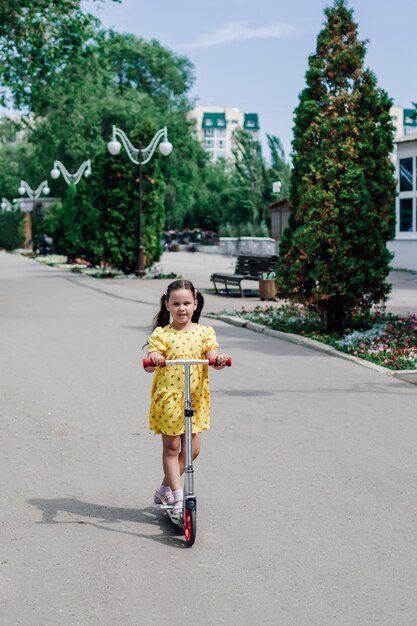 Une jolie fille vêtue d'une robe jaune apprend à faire du scooter dans la ville et profite d'une chaude journée d'été