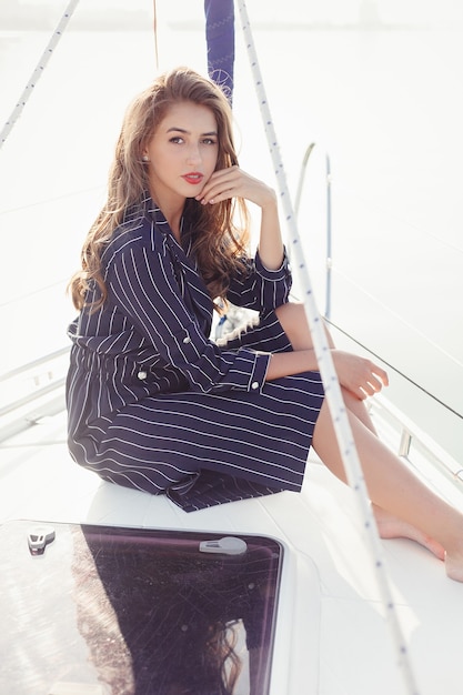 Jolie fille sur un yacht au jour d'été. Gros plan du portrait de mode de superbe femme romantique posant yacht. Vêtu d'une robe élégante, tenue d'été. Ciel bleu. le coucher du soleil
