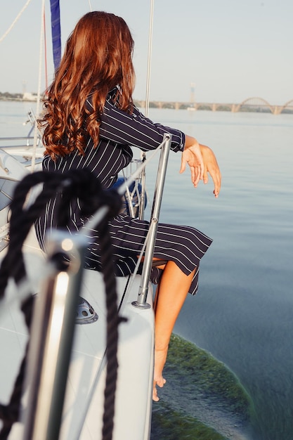 Jolie fille sur un yacht au jour d'été. Gros plan du portrait de mode d'une superbe femme romantique posant un yacht. Vêtue d'une robe élégante, tenue d'été. Ciel bleu. le coucher du soleil