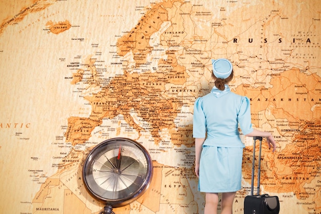 Jolie hôtesse de l'air appuyée sur une valise contre une carte du monde avec une boussole montrant l'europe et le moyen-orient