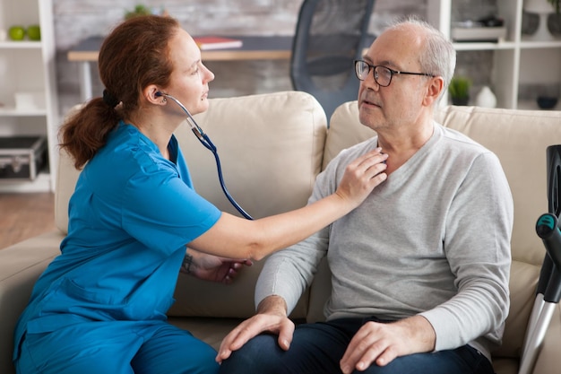 Jolie infirmière utilisant un stéthoscope pour écouter le cœur d'un vieil homme dans une maison de retraite.