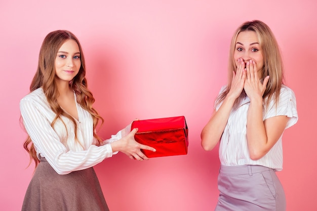 Jolie et jeune adolescente donnant une boîte avec un cadeau pour ravir la maman surprise sur fond rose en studio. le concept de célébrer la fête des mères et l'anniversaire