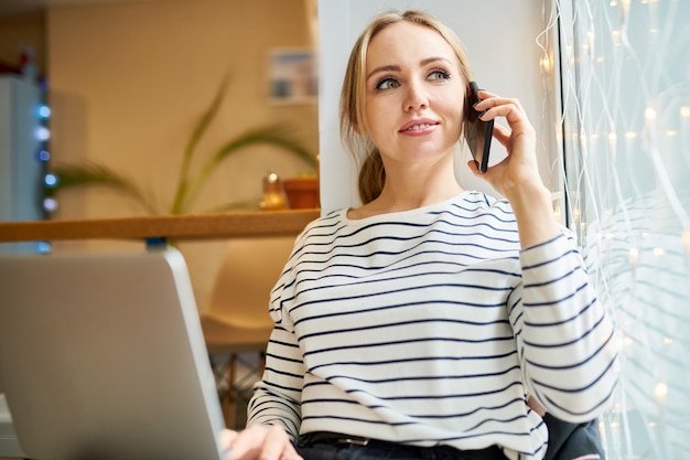 Jolie jeune agent avec smartphone et ordinateur portable consultant l'un de ses clients assis dans un café