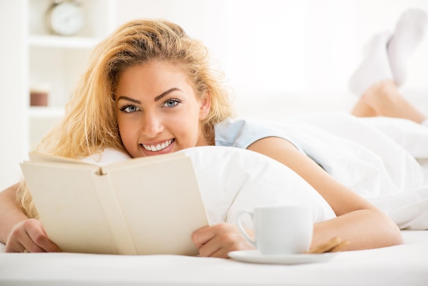 Jolie jeune belle femme lisant un livre dans le lit