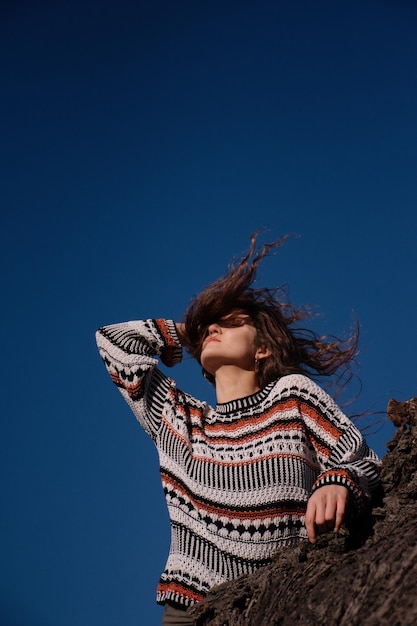 Jolie jeune brune aux cheveux longs contre un ciel bleu ensoleillé.