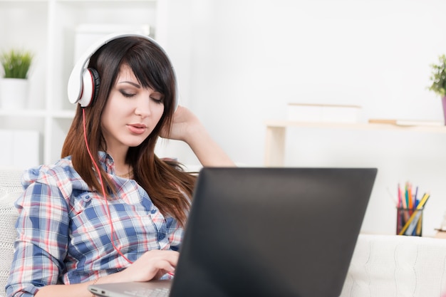 Jolie jeune brune écoute de la musique et tapant dans un ordinateur portable