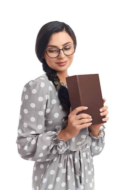 Jolie jeune brune à lunettes et robe posant sur fond blanc avec des livres.