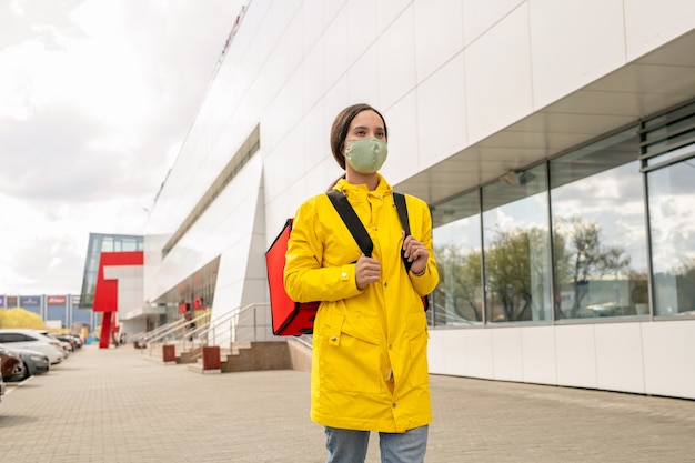 Jolie jeune courrier en trench jaune et masque de protection