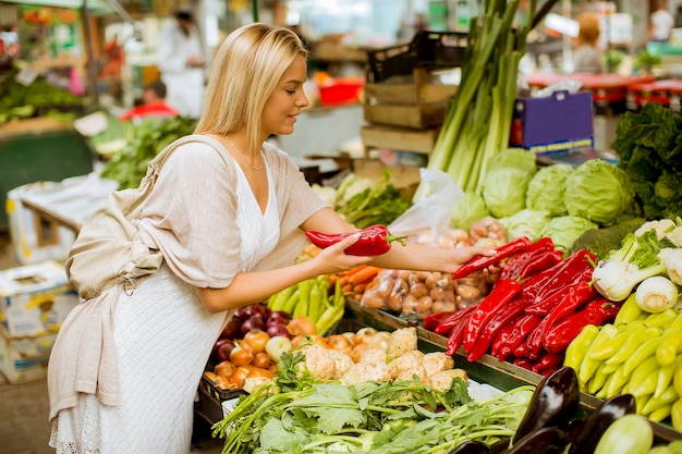 Jolie jeune femme achète des légumes au marché