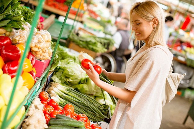 Jolie jeune femme achète des légumes au marché