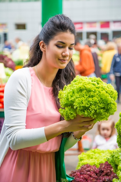 Jolie jeune femme achète des légumes sur le marché