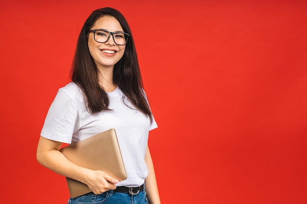 Jolie jeune femme d'affaires décontractée tenant un ordinateur portable au bureau isolé sur fond rouge