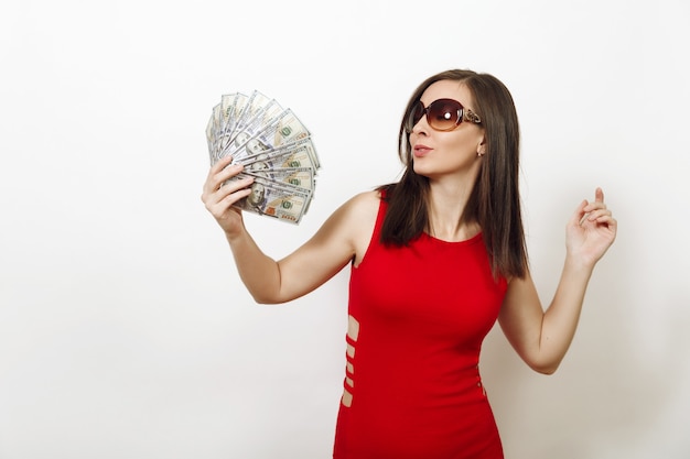 Jolie jeune femme d'affaires heureuse caucasienne en robe rouge ajustée et lunettes tenant des billets d'argent sur fond blanc. Belle fille avec de l'argent à côté isolé.