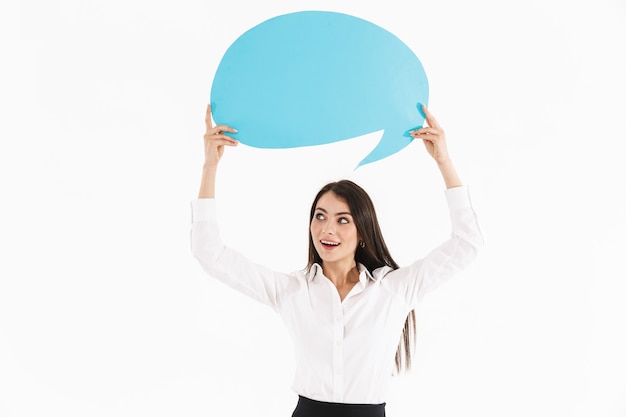 Jolie jeune femme d'affaires heureuse debout isolée sur un mur blanc, montrant une bulle de dialogue vide