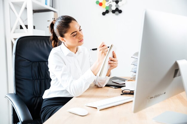 Jolie jeune femme d'affaires prenant des notes alors qu'elle était assise sur le lieu de travail au bureau