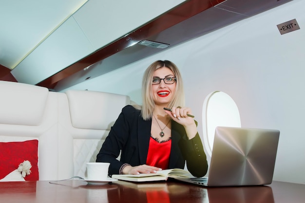 Jolie jeune femme d'affaires travaillant sur ordinateur portable en jet privé de luxe. Femme d'affaires en siège de première classe d'avion pendant le voyage. Concept de qualité du service aux passagers dans l'industrie aéronautique, voyage au plus haut