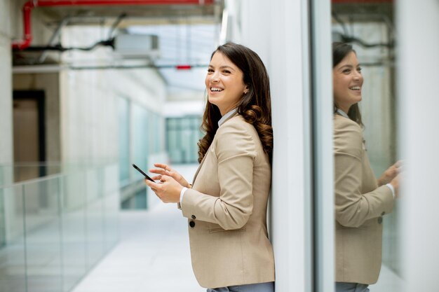 Jolie jeune femme d'affaires utilisant un téléphone portable dans le couloir du bureau