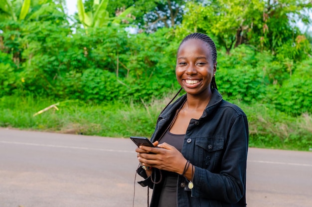 Jolie jeune femme africaine souriante et utilisant son téléphone portable en plein air