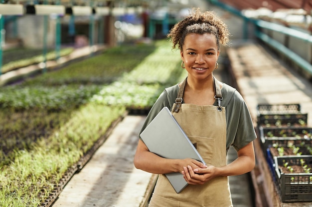 Photo jolie jeune femme afro-américaine avec ordinateur portable debout dans une serre