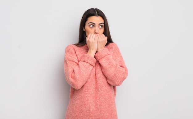 Jolie jeune femme à l'air inquiète, anxieuse, stressée et effrayée, se rongeant les ongles et regardant vers l'espace de copie latéral