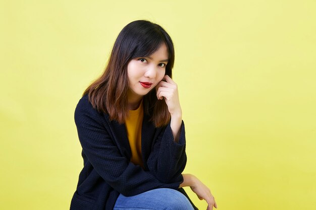 Jolie jeune femme asiatique assise sur la boîte vide vide sur jaune