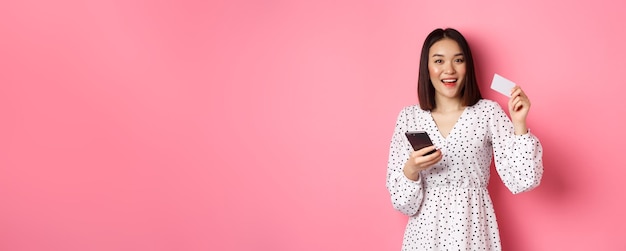 Jolie jeune femme asiatique commande en ligne tenant une carte de crédit et un téléphone portable faisant l'achat d'internet