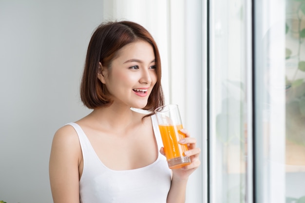 Jolie jeune femme asiatique dans une pièce lumineuse buvant du jus d'orange