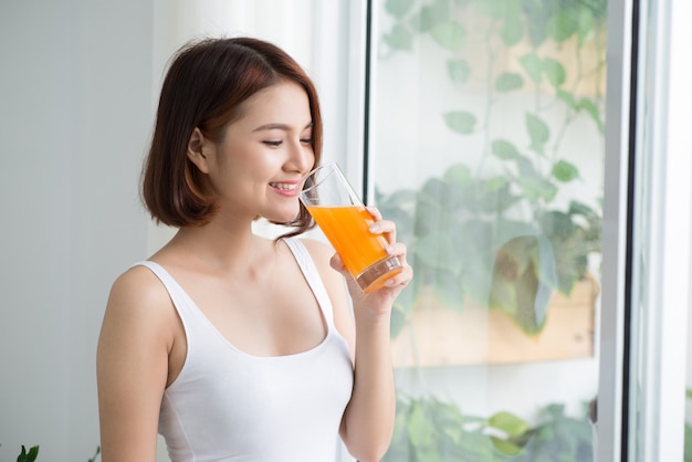 Jolie jeune femme asiatique dans une pièce lumineuse buvant du jus d'orange