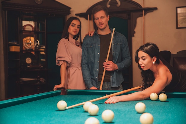 Jolie jeune femme asiatique joue au jeu de billard. Elle a l'air noce et concentrée. Ses amis se tiennent d'ailleurs. Ils la regardaient jouer.