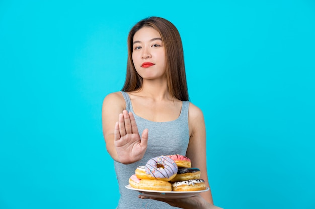 Jolie jeune femme asiatique ne faisant aucune action avec des beignets sur le mur de couleur bleu isolé