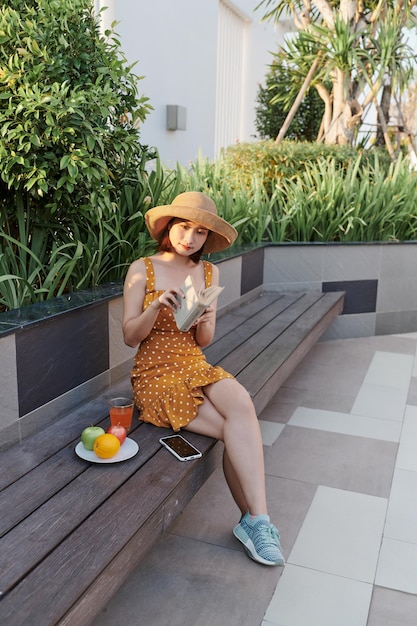 Jolie jeune femme assise dans le parc et lisant le livre