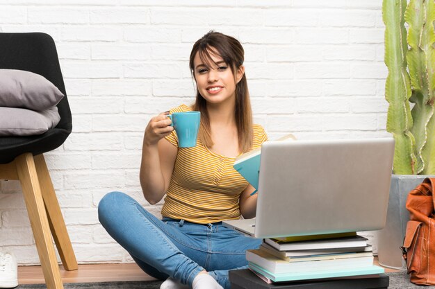 Jolie jeune femme assise sur le sol à l&#39;intérieur tenant une tasse de café