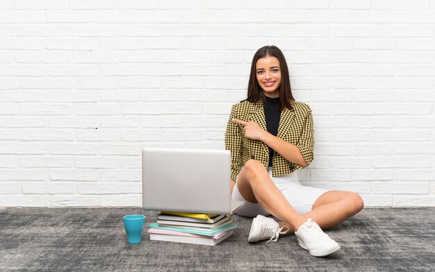 Jolie jeune femme assise sur le sol pointant sur le côté pour présenter un produit