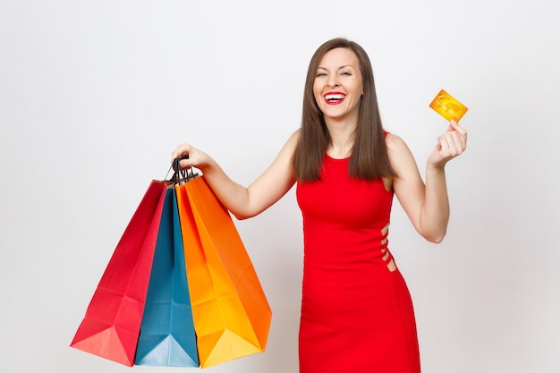 Jolie jeune femme aux cheveux bruns à la mode glamour en robe rouge tenant une carte de crédit, des paquets multicolores avec des achats après le shopping isolés sur fond blanc. Copiez l'espace pour la publicité.