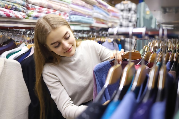 Jolie jeune femme aux cheveux longs choisit des vêtements dans un concept de magasin de vente de mode shopping