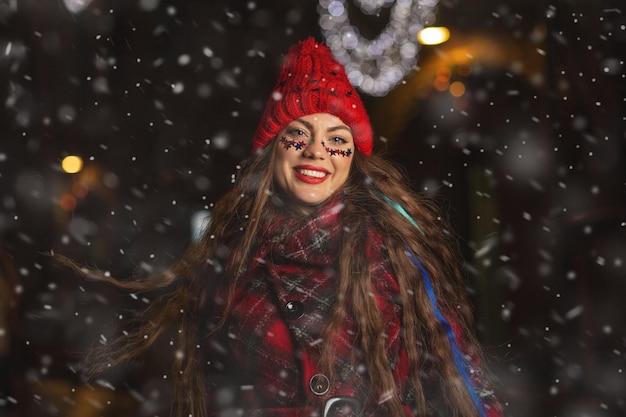 Jolie jeune femme aux cheveux longs profitant du temps neigeux à la foire de Noël