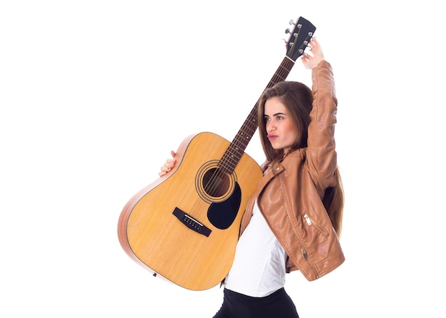 Jolie jeune femme aux cheveux longs en veste marron et pantalon noir tenant une guitare sur fond blanc en studio