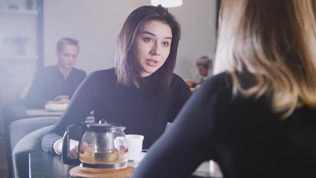 Jolie jeune femme aux cheveux noirs, boire du café et parler avec sa petite amie dans le café, portrait