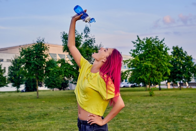 Jolie jeune femme aux cheveux roses se verse sexuellement de l'eau après l'entraînement