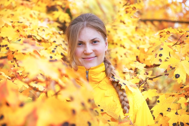 Jolie jeune femme aux cheveux rouges dans le parc en automne avec des feuilles tombées jaunes