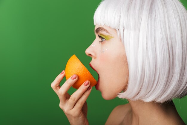 Jolie Jeune Femme Aux Seins Nus Portant Des Cheveux Blancs Courts Debout Isolé, Manger Des Tranches D'orange