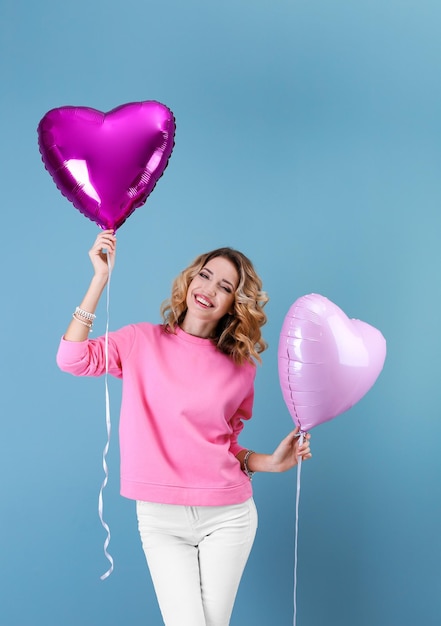 Jolie jeune femme avec des ballons à air en forme de coeur sur un fond de couleur