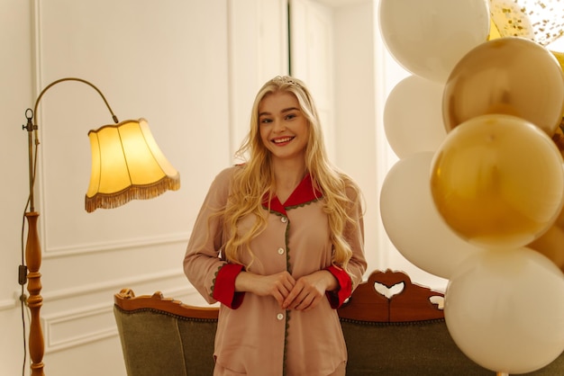 Jolie jeune femme blonde caucasienne en pyjama sourit à la caméra avec des ballons pour son concept de vacances d'anniversaire