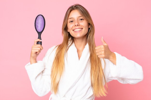 Jolie jeune femme blonde portant un peignoir et tenant une brosse à cheveux